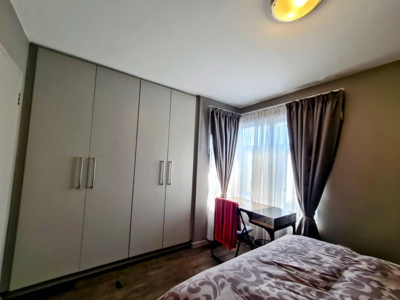 A well-maintained bedroom featuring extensive built-in floor-to-ceiling cabinetry and wood-look flooring, offering ample storage and a neutral color palette.