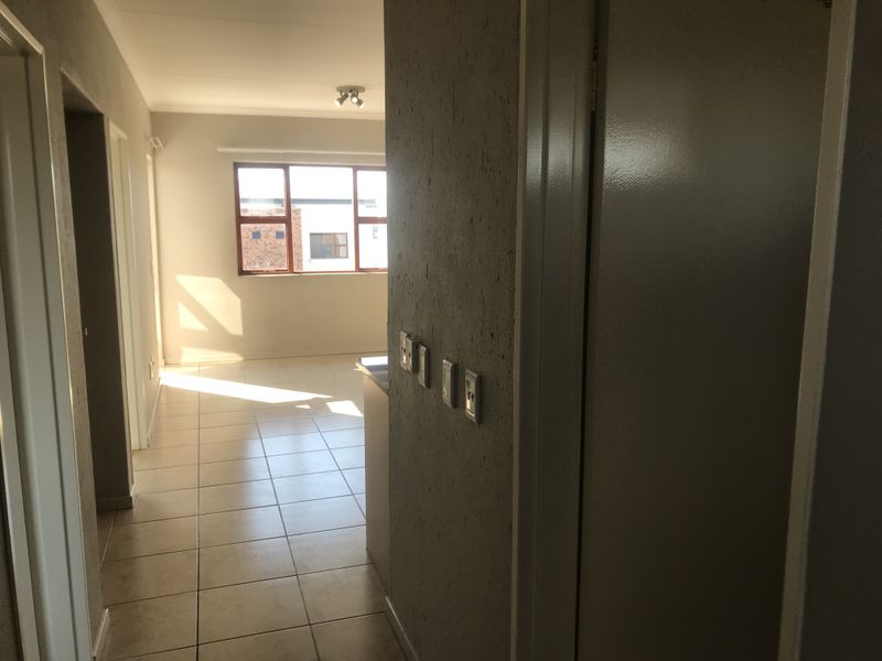 A view through a hallway with tiled flooring and textured walls, leading towards an open living area with natural light.