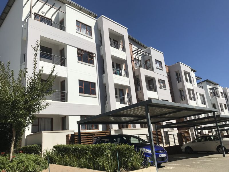 A modern multi-story apartment complex featuring white facade finishes, private balconies, and dedicated covered parking bays for residents.