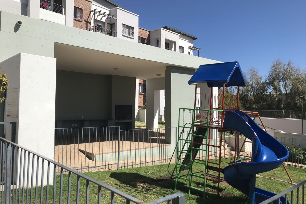 Communal outdoor area featuring a covered patio with a built-in braai and an adjacent playground with a slide and climbing frame.
