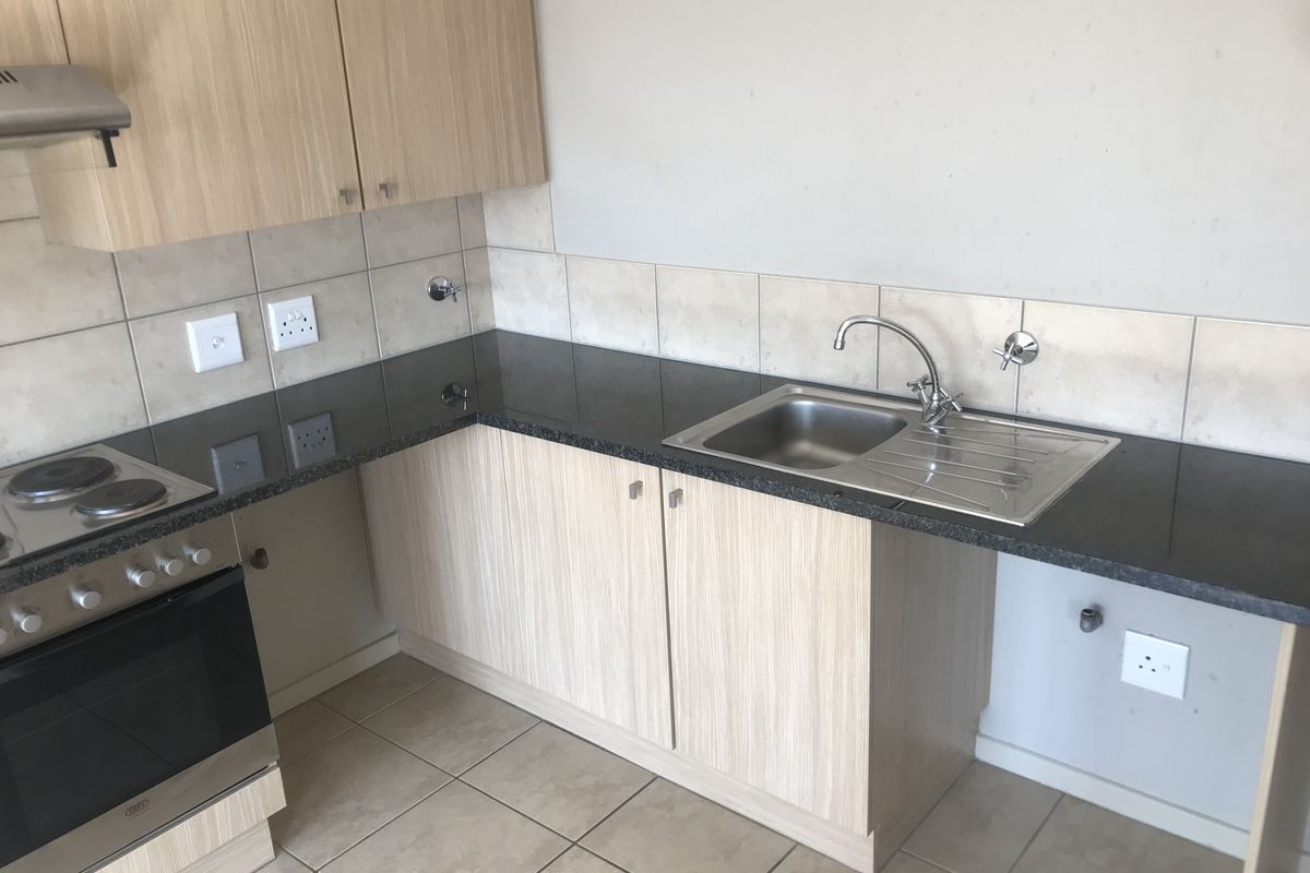 A functional kitchen featuring light wood-finish cabinetry, dark granite countertops, a stainless steel sink, and a built-in electric stove with an extractor fan.
