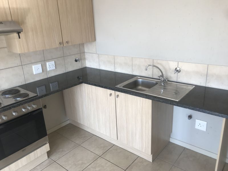 A functional kitchen featuring light wood-finish cabinetry, dark granite countertops, a stainless steel sink, and a built-in electric stove with an extractor fan.