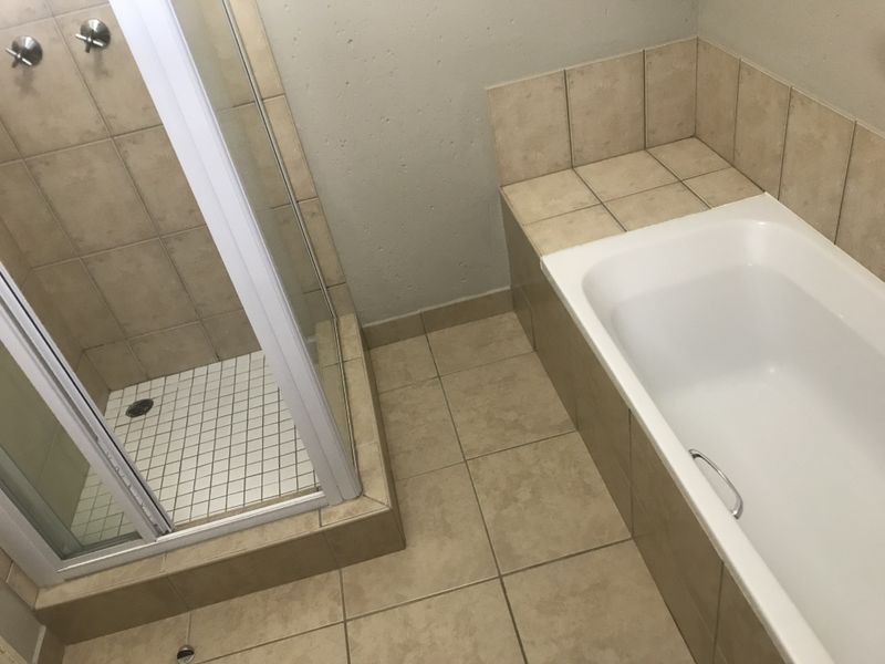 A functional bathroom featuring a separate shower enclosure and a built-in bathtub with neutral ceramic tiling throughout.