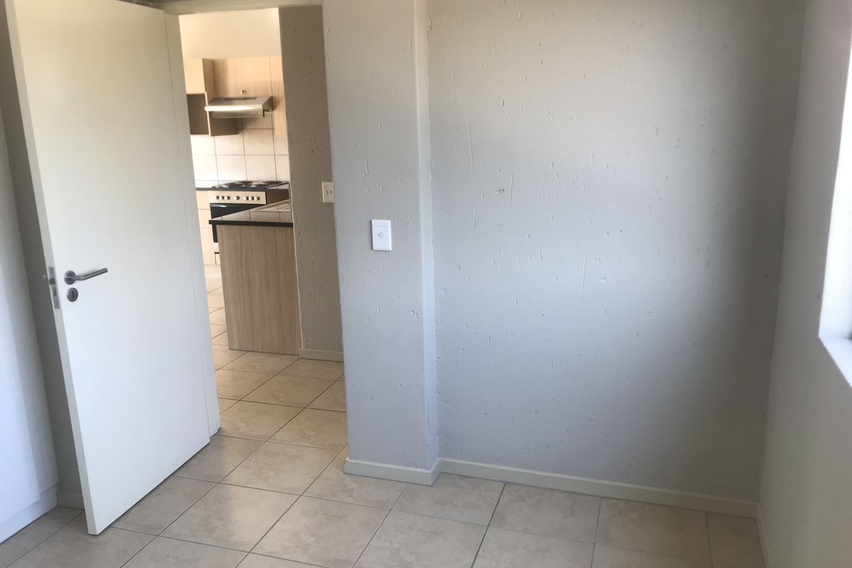 An empty living area with tiled flooring and a doorway leading to a kitchen, featuring neutral wall finishes.