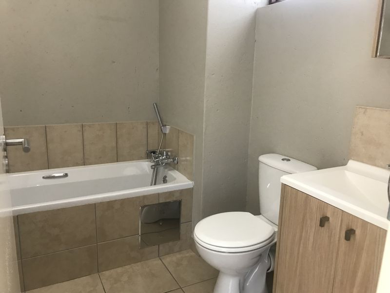 A functional bathroom featuring a bathtub with handheld shower, a standard toilet, and a vanity cabinet with a basin.
