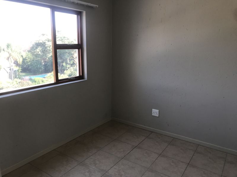 An empty bedroom featuring tiled flooring, a window with a wooden frame, and neutral wall finishes, offering a blank canvas for personalization.