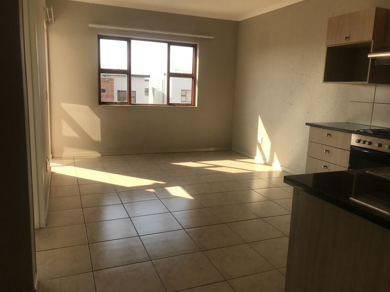 An empty open-plan living and kitchen area featuring tiled floors, built-in cabinetry, and a built-in oven and hob.