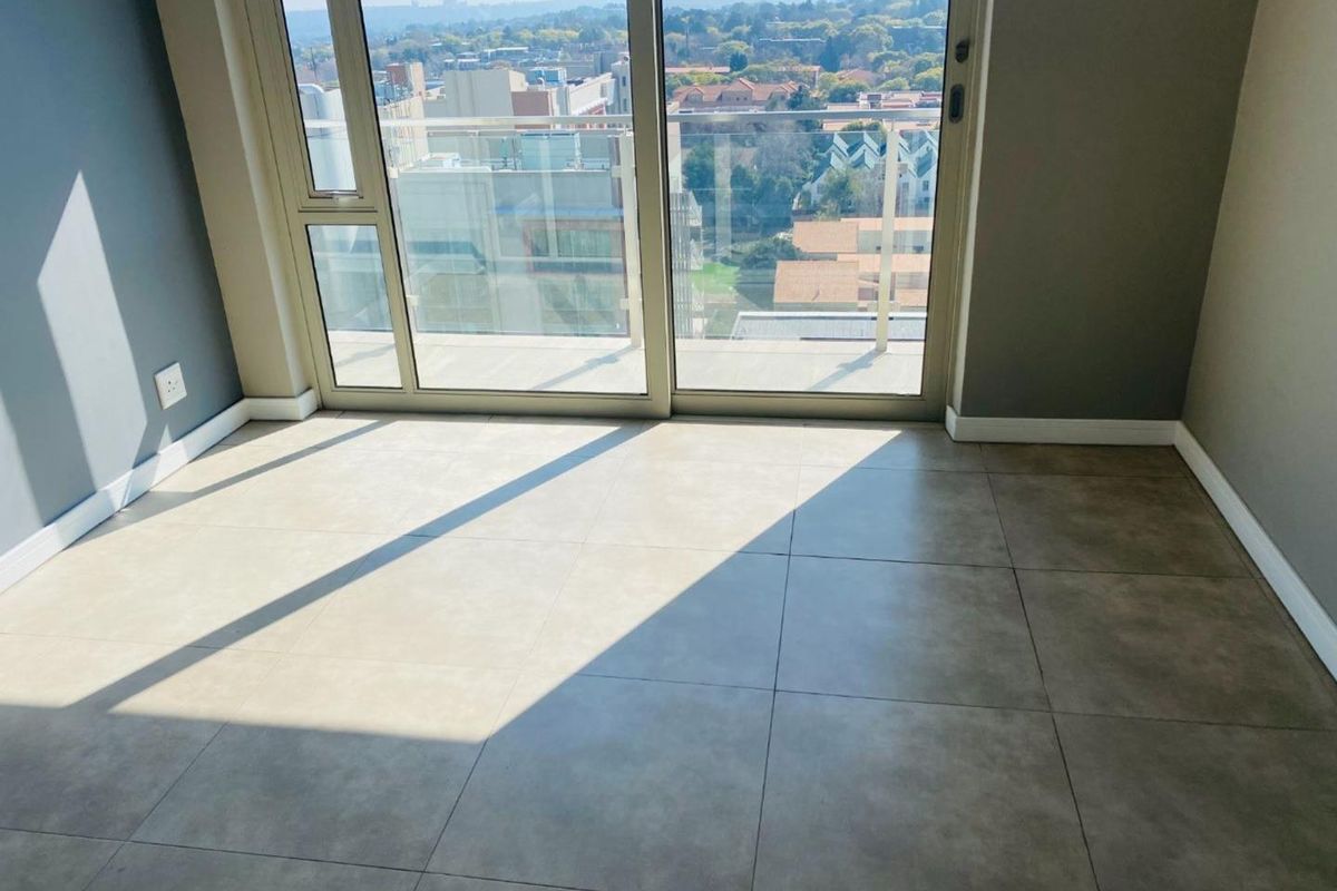 A bright, empty living area featuring large format floor tiles and expansive sliding glass doors that open onto a balcony with city views.