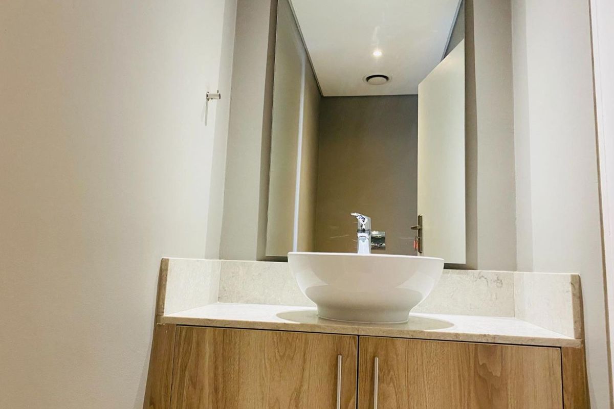 A modern bathroom vanity featuring a white vessel sink, stone countertop, and wooden cabinetry with a large integrated mirror.