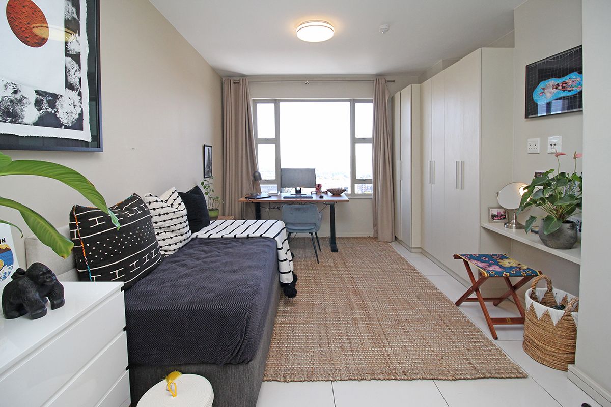 A well-lit bedroom featuring built-in floor-to-ceiling wardrobes, a dedicated desk area, and large windows providing natural light and city views.
