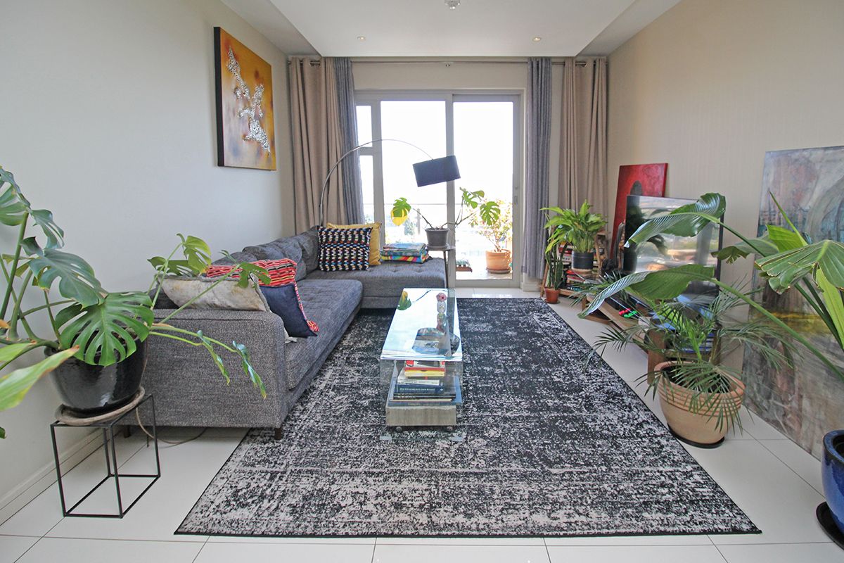 A bright living room featuring large sliding glass doors that open onto a balcony, with neutral tiled flooring and recessed ceiling lighting.