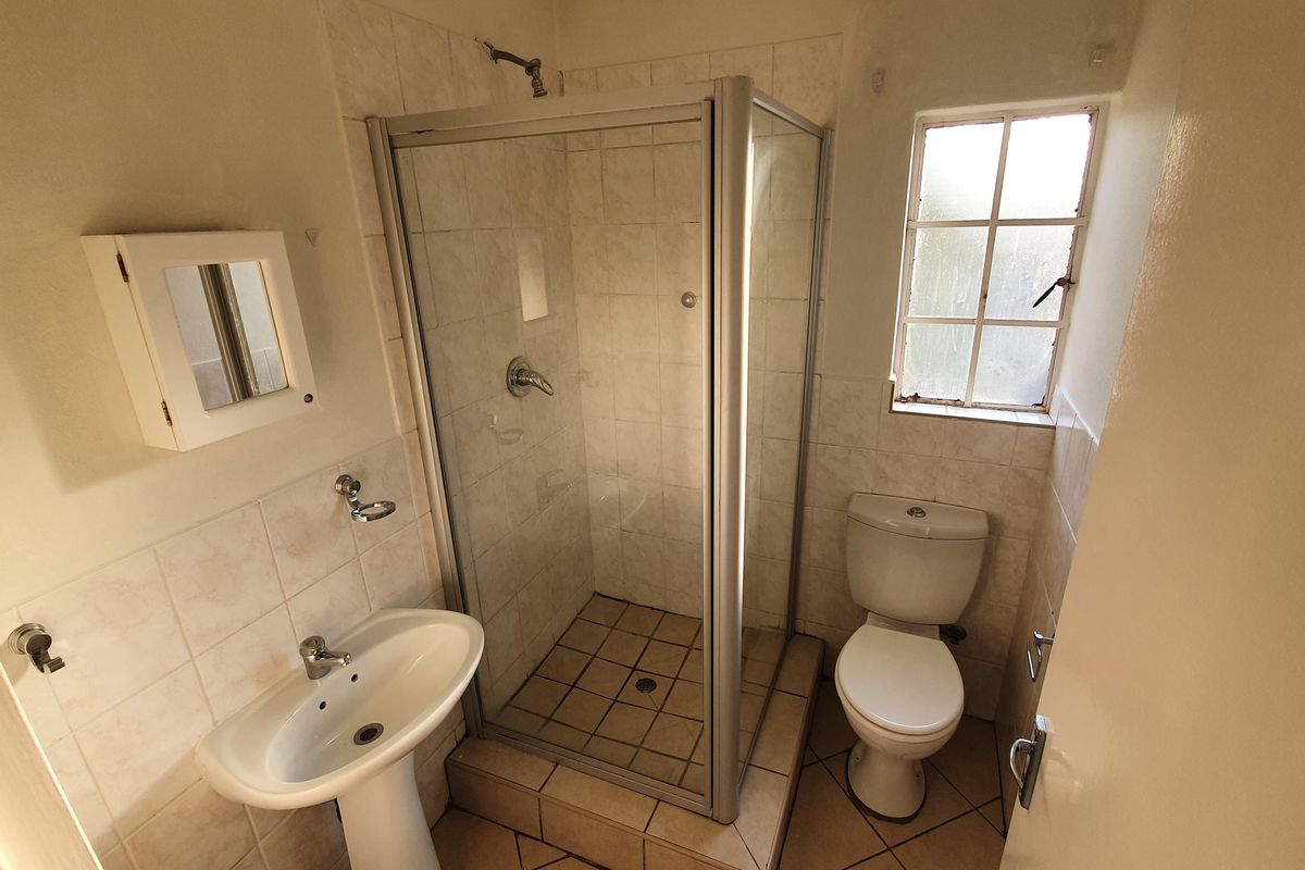 A functional bathroom featuring a corner shower enclosure, pedestal basin, and toilet, finished with neutral wall and floor tiling.