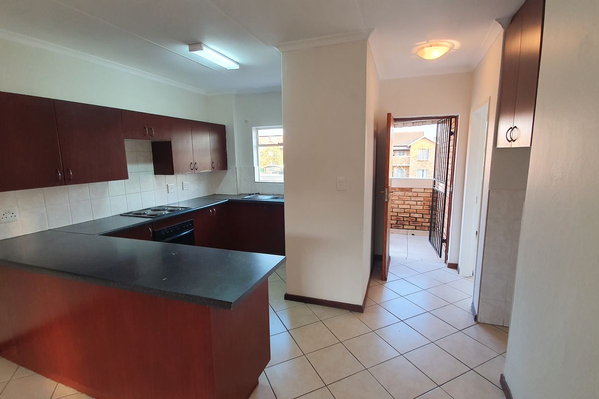 Functional kitchen featuring dark wood cabinetry, laminate countertops, built-in hob and oven, with tiled flooring and direct access to an exterior balcony.