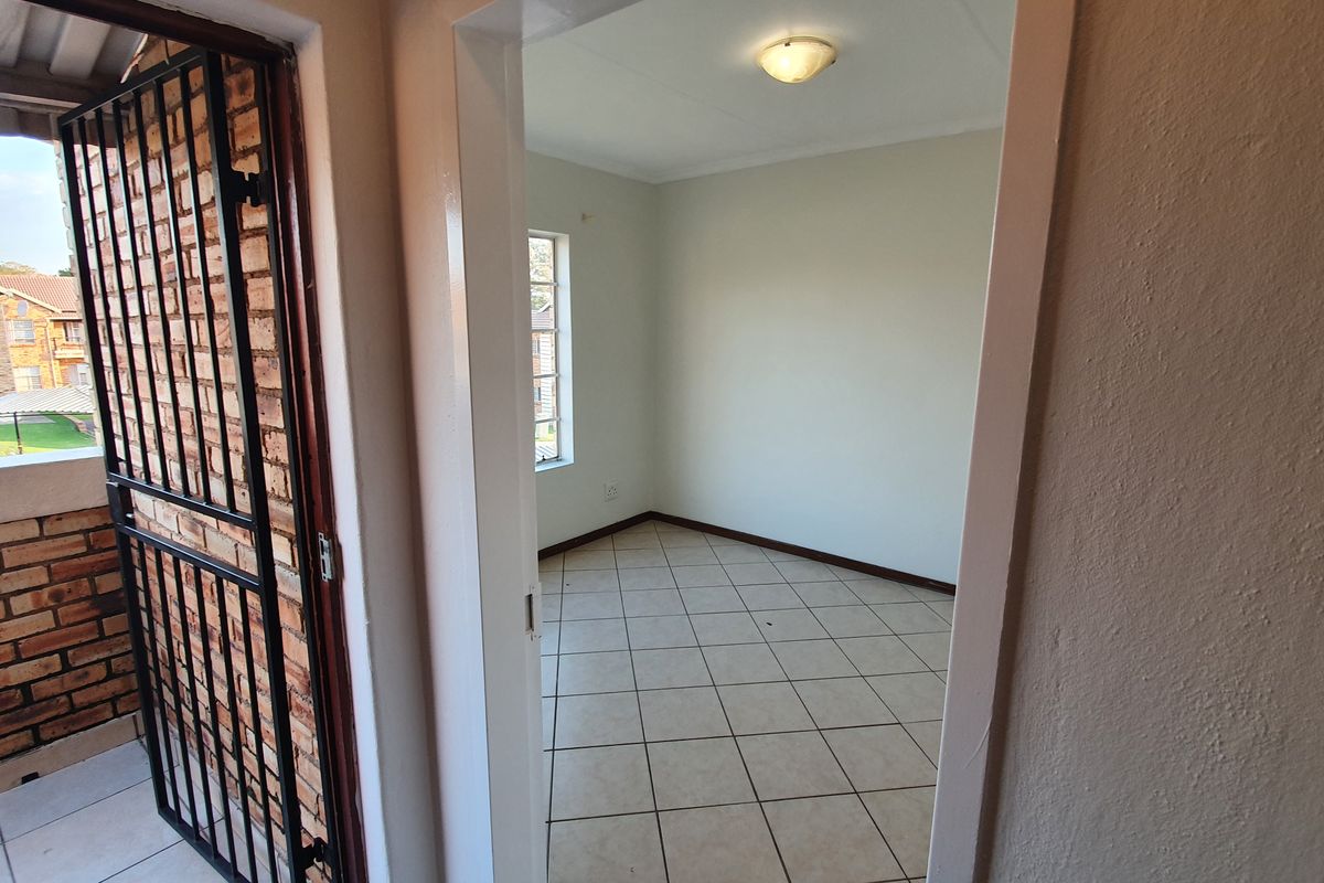 A view from a balcony into an empty bedroom featuring tiled flooring and a window, providing a neutral space ready for personalization.