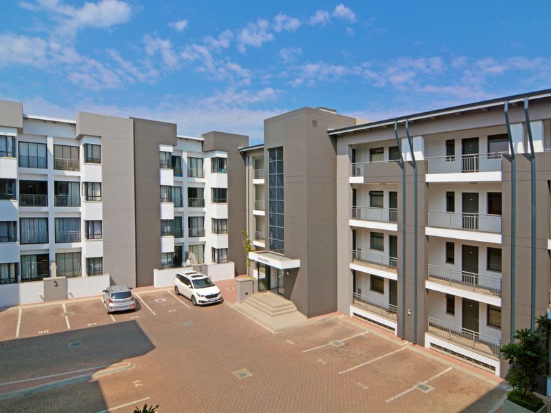 Exterior view of a modern multi-story apartment complex featuring paved parking, structured facades, and balcony access.