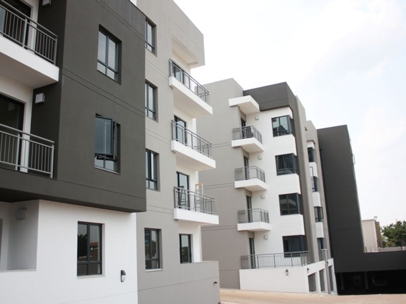 Modern multi-story apartment complex featuring contemporary grey and white facade, private balconies with metal railings, and large aluminium-framed windows.