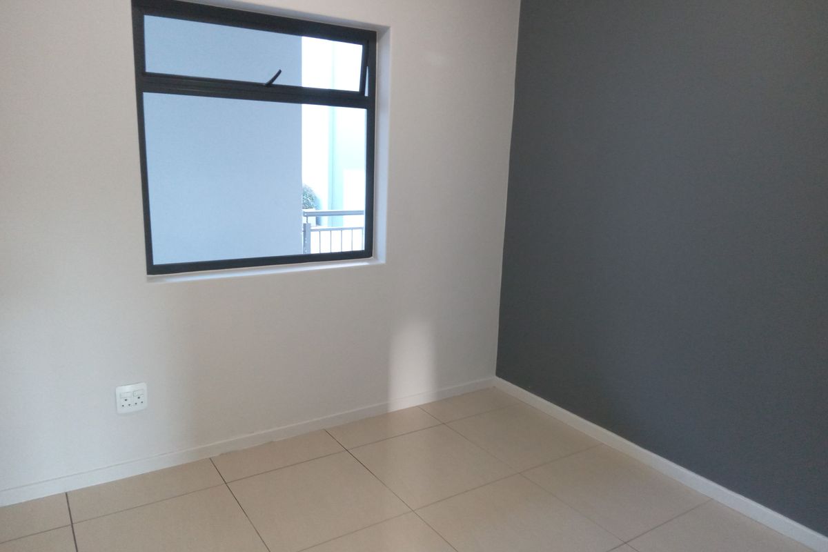 A clean, empty bedroom featuring neutral tiled flooring, a modern aluminium window, and a contrasting dark grey feature wall.