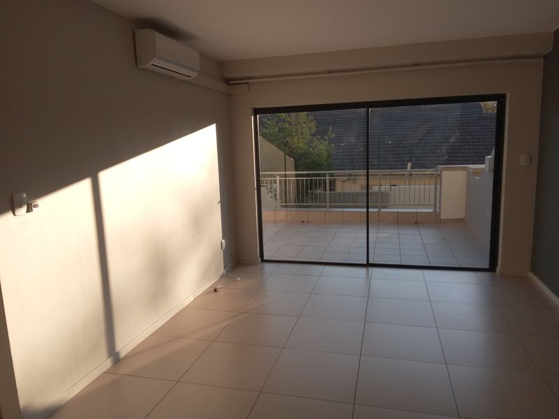 Bright and spacious living area featuring neutral tiled flooring, a wall-mounted air conditioning unit, and large sliding glass doors opening onto a private balcony.