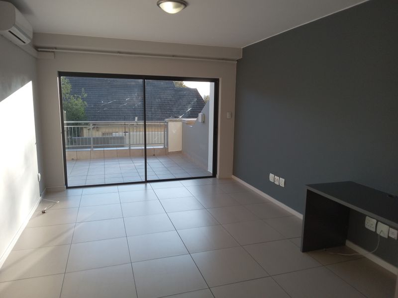 A bright, empty living area featuring neutral tiled flooring, a modern accent wall, built-in desk, and large sliding doors leading to a private balcony.