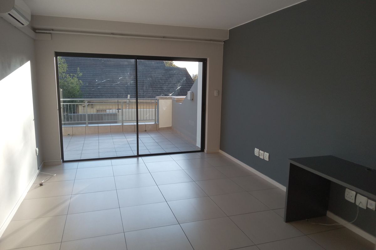 A bright, empty living area featuring neutral tiled flooring, a modern accent wall, built-in desk, and large sliding doors leading to a private balcony.