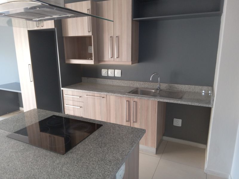 Modern kitchen featuring light wood cabinetry, granite countertops, a central island with an integrated electric hob, and a stainless steel sink.