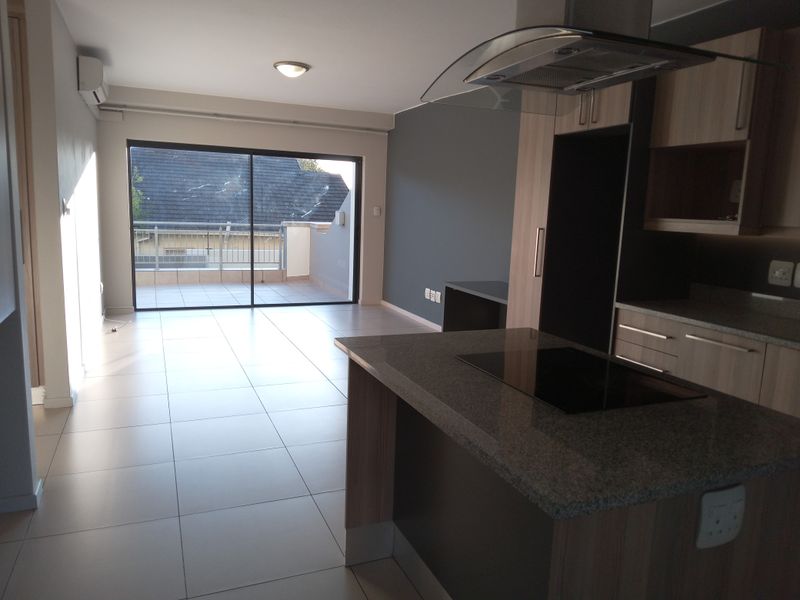 Modern open-plan living area featuring a sleek kitchen with stone countertops, built-in hob, extractor fan, and direct access to a private balcony.