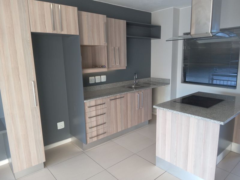 Modern kitchen featuring light wood-grain cabinetry, granite countertops, a central island with an integrated hob, and stainless steel extractor fan.