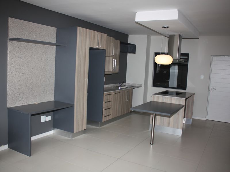 Modern open-plan kitchen and living area featuring contemporary cabinetry, stone countertops, integrated appliances, and sleek tiled flooring.