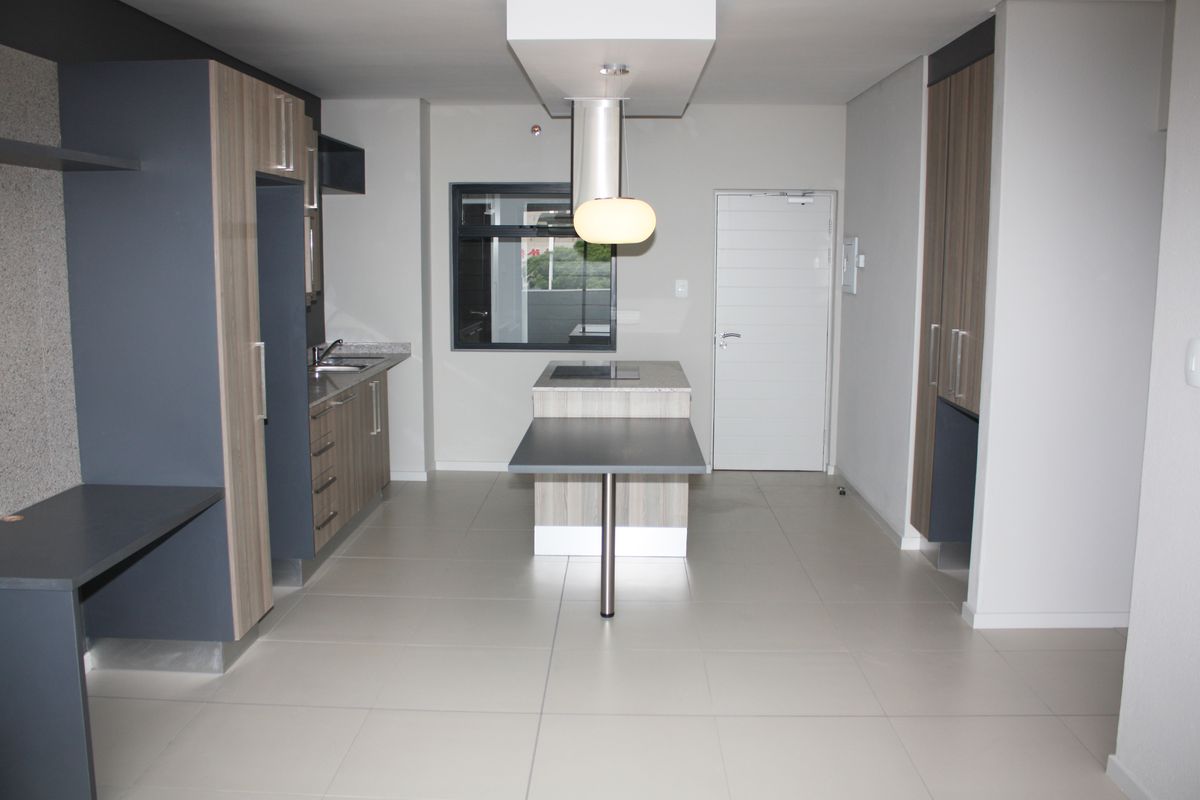 Modern kitchen featuring a central island with integrated hob, sleek cabinetry, tiled flooring, and contemporary pendant lighting in an open-plan layout.