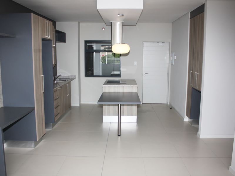 Modern kitchen featuring a central island with integrated hob, sleek cabinetry, tiled flooring, and contemporary pendant lighting in an open-plan layout.