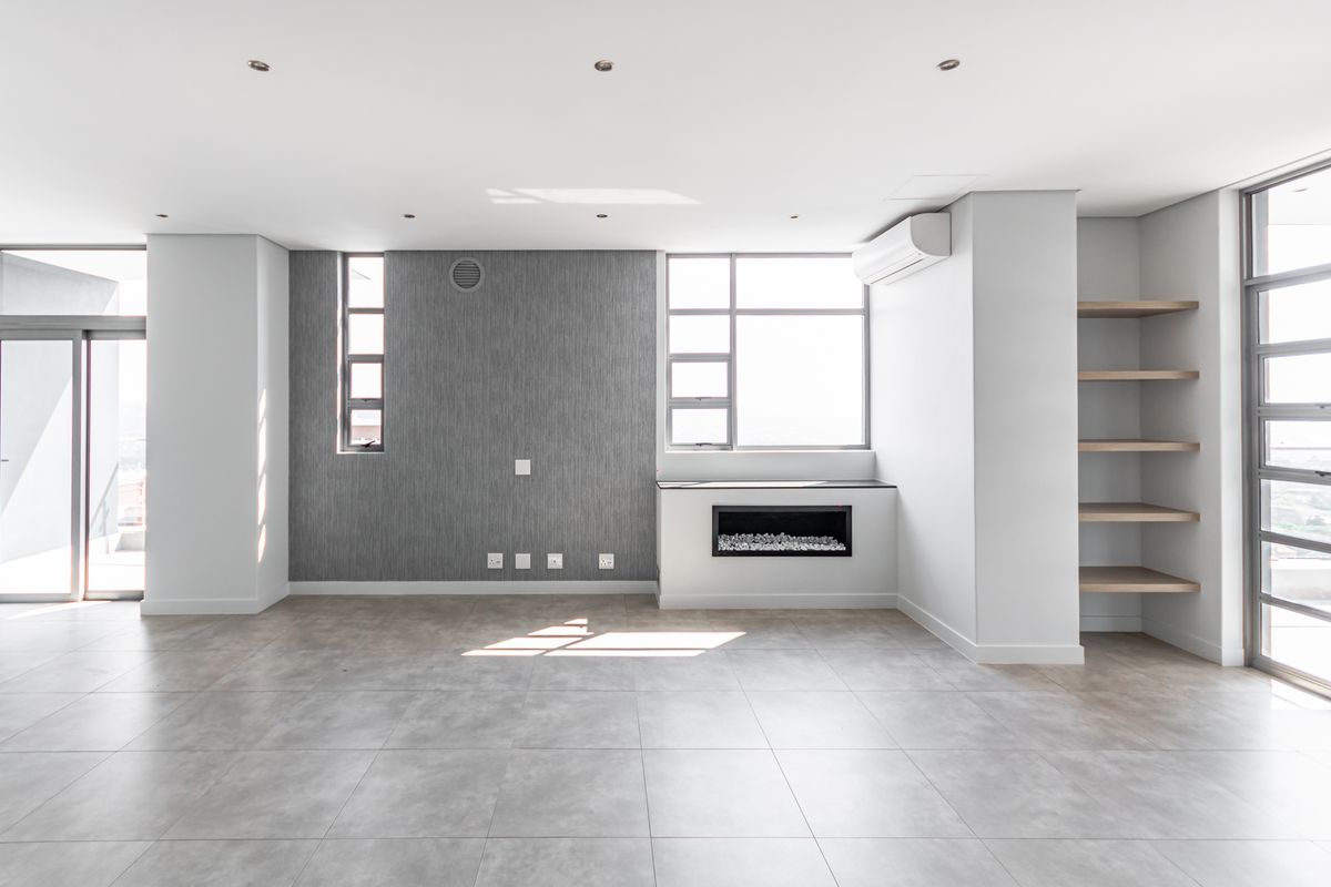 A bright, modern, and empty living area featuring tiled floors, a built-in fireplace, integrated shelving, and large windows with access to a balcony.