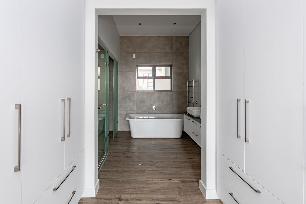 Modern bathroom featuring a freestanding bathtub, vessel sink, heated towel rail, and glass shower enclosure, flanked by ample built-in storage cupboards.