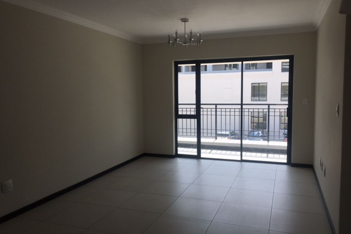 Spacious open-plan living area featuring neutral tiled flooring, crown molding, and large sliding glass doors leading to a private balcony.