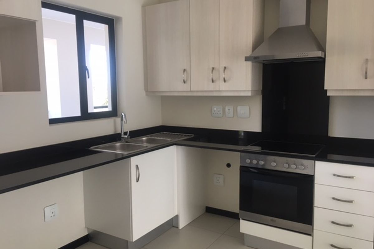 Modern kitchen featuring light wood cabinetry, black granite countertops, stainless steel oven, hob, and extractor fan with tiled flooring.