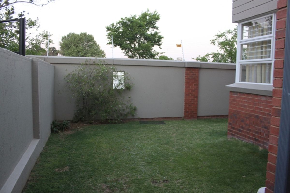 A private rear garden area featuring a well-maintained lawn, enclosed by a secure perimeter wall with electric fencing and brick detailing.