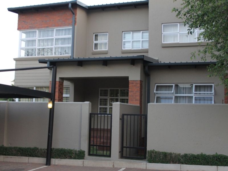 Front elevation of a modern apartment building featuring brick accents, a secure gated entrance, and a covered carport.