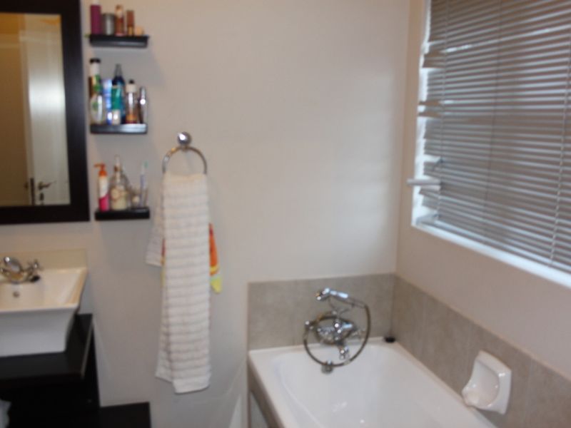 A functional bathroom featuring a vessel sink vanity, a bathtub with chrome fixtures, and venetian blinds for privacy.