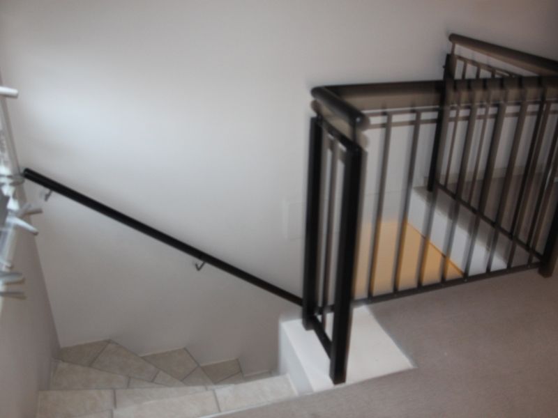 A staircase featuring tiled treads and a modern black metal balustrade with a matching handrail, connecting levels within the apartment.
