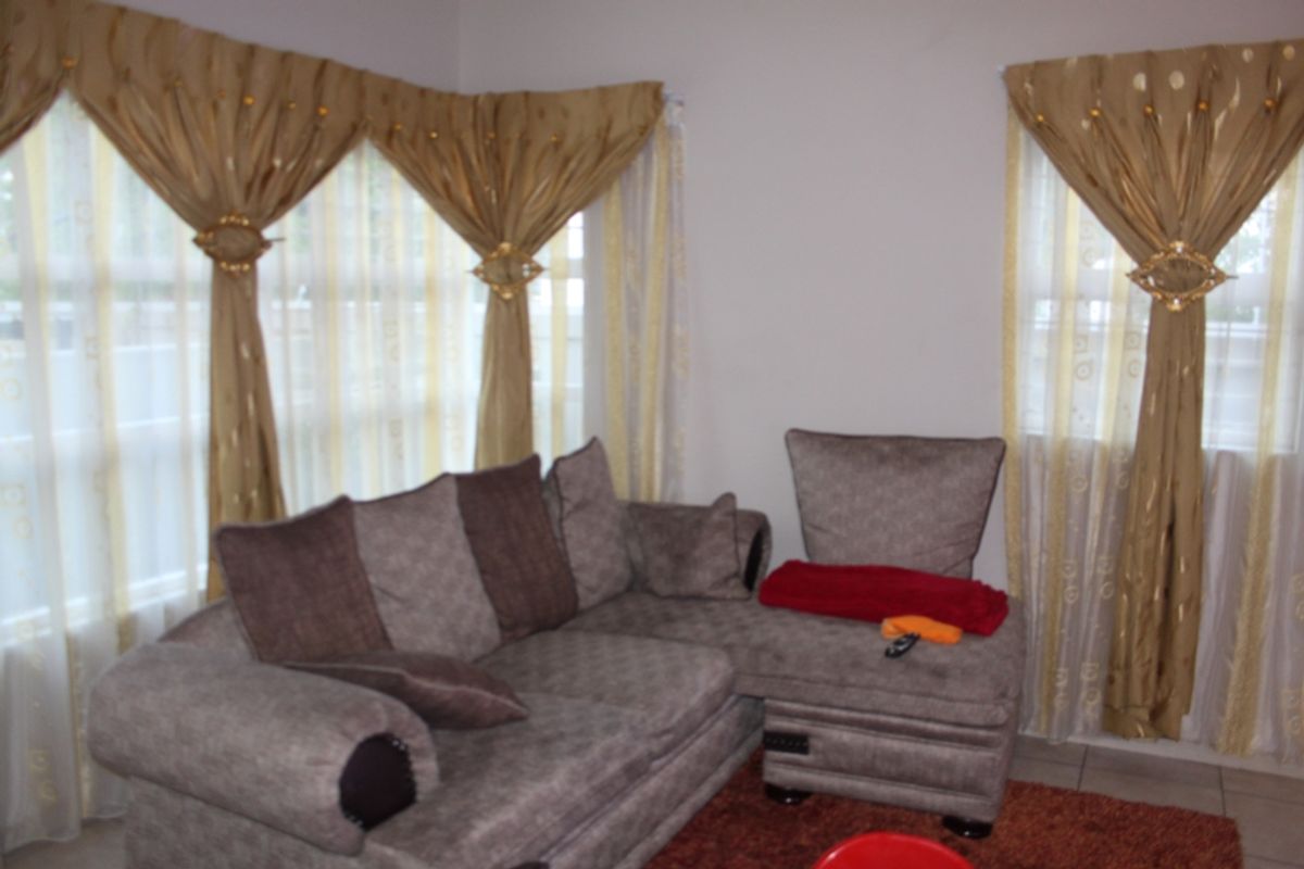 A living room area featuring tiled flooring and large windows with decorative curtains.