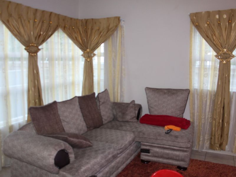 A living room area featuring tiled flooring and large windows with decorative curtains.