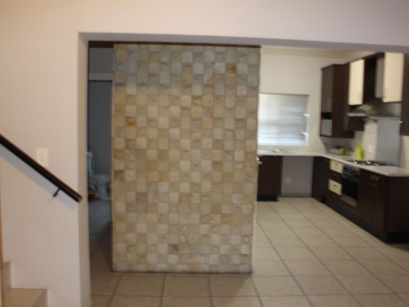 Open plan kitchen area featuring a stone feature wall, dark cabinetry, built-in oven and hob, and tiled flooring.