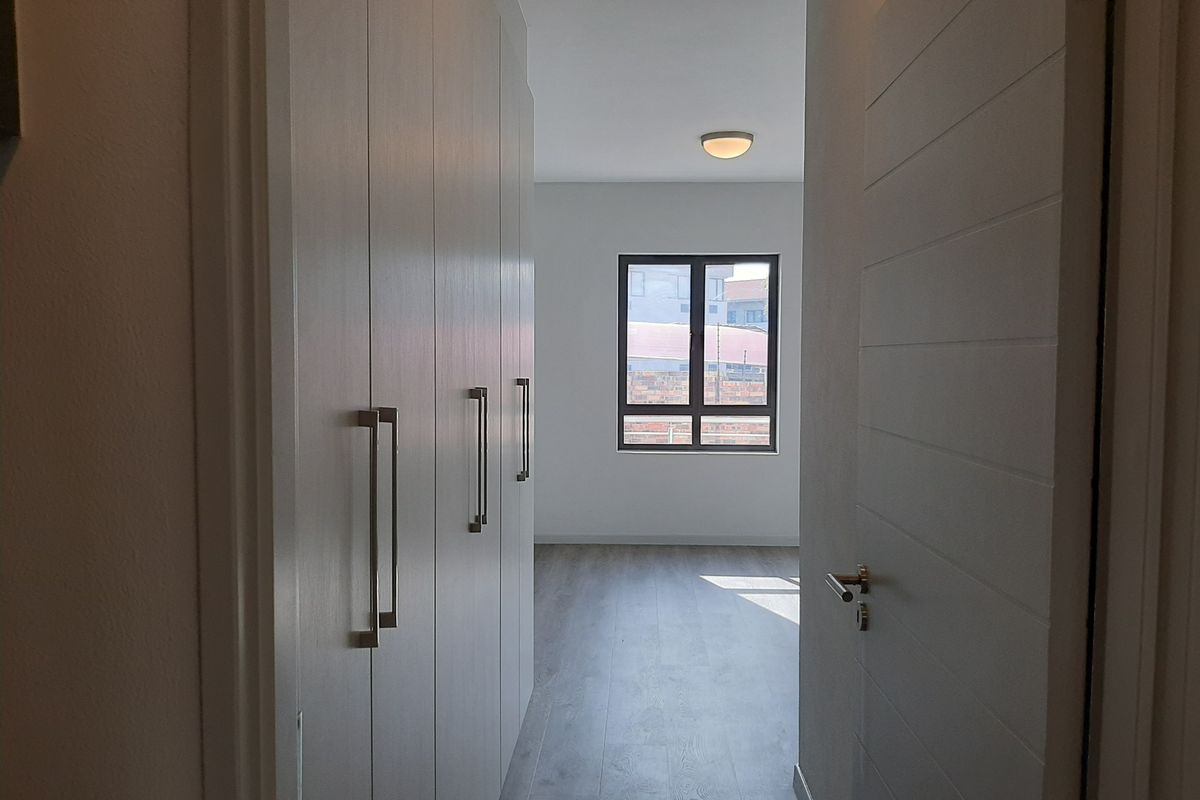 A bright bedroom featuring built-in wardrobes, modern laminate flooring, and a window providing natural light.