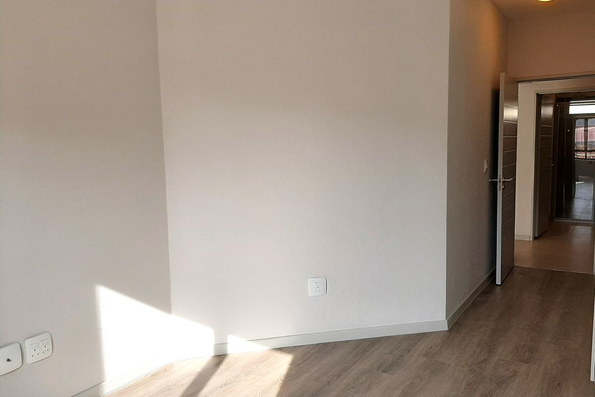 A bright, empty living area featuring modern wood-look laminate flooring, neutral walls, and a doorway leading to an adjacent room.
