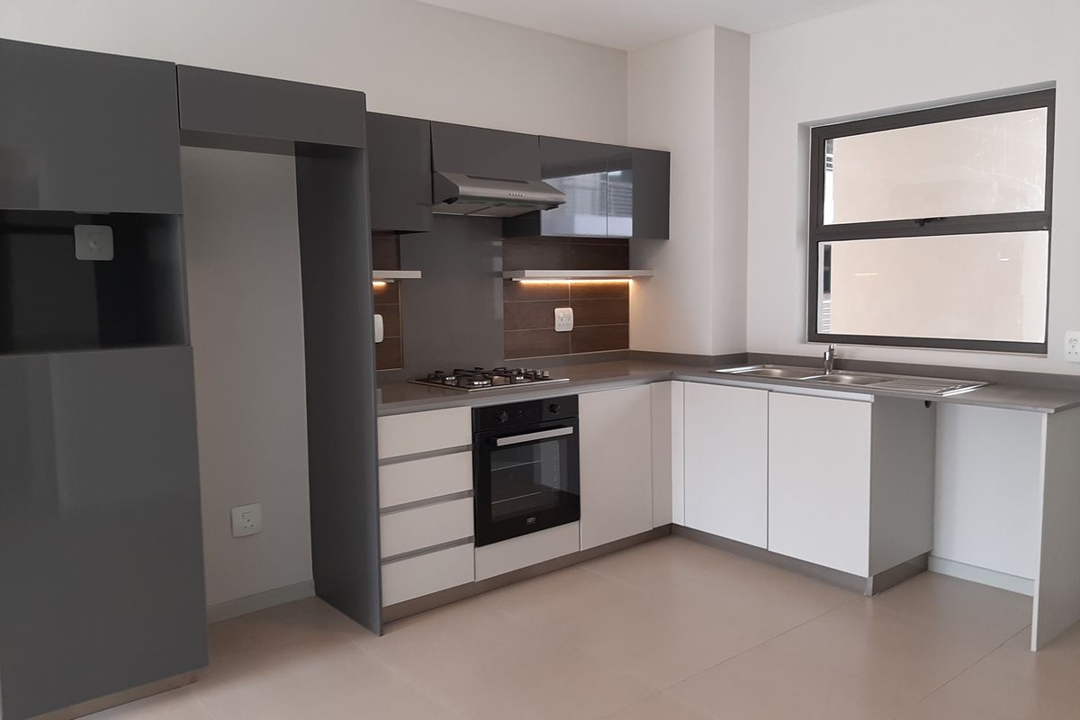 Modern kitchen featuring sleek two-tone cabinetry, built-in oven, gas hob, extractor fan, and a double sink with tiled flooring.