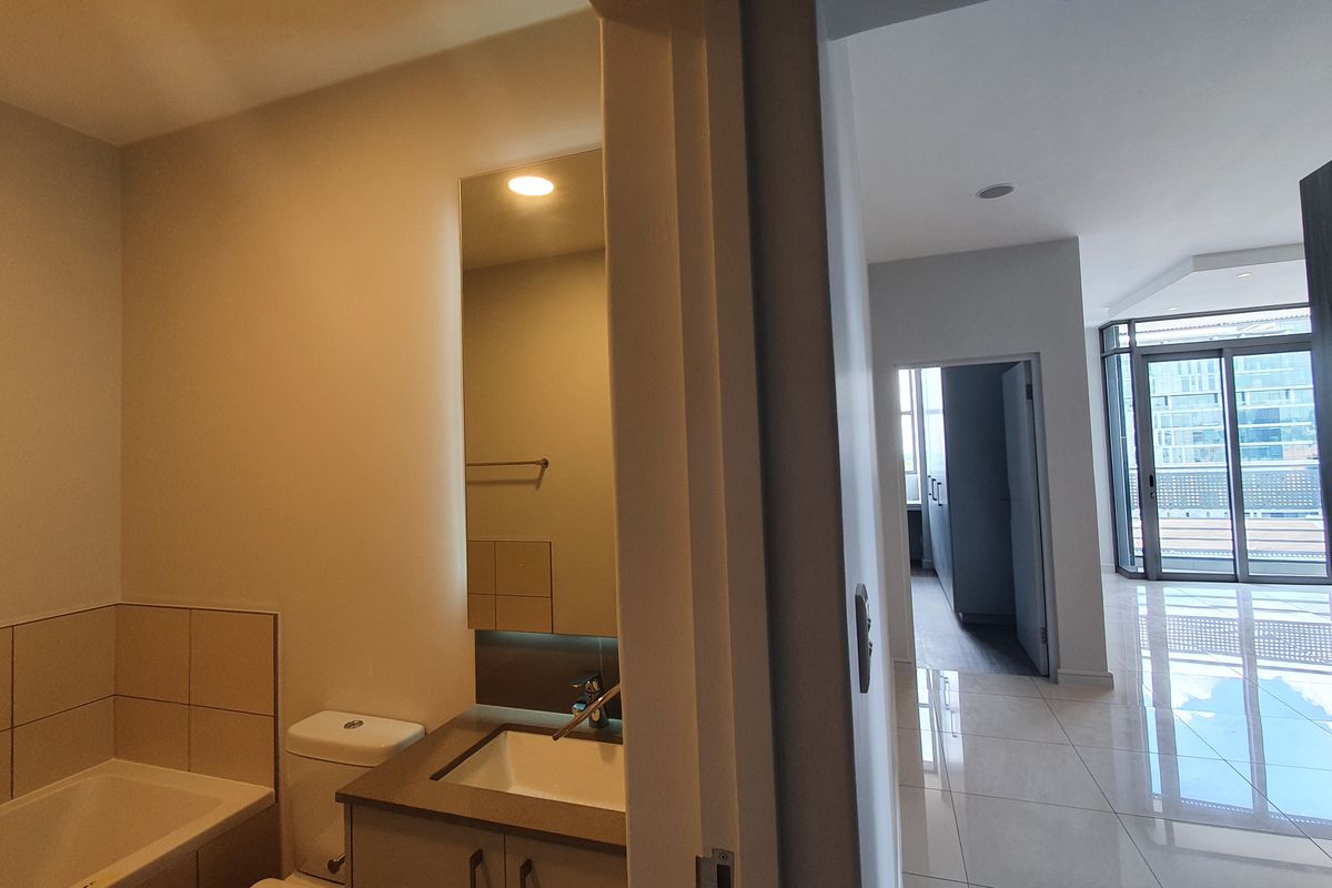 A clean, modern bathroom featuring a built-in vanity, integrated basin, toilet, and bathtub, with neutral tiling and recessed lighting.