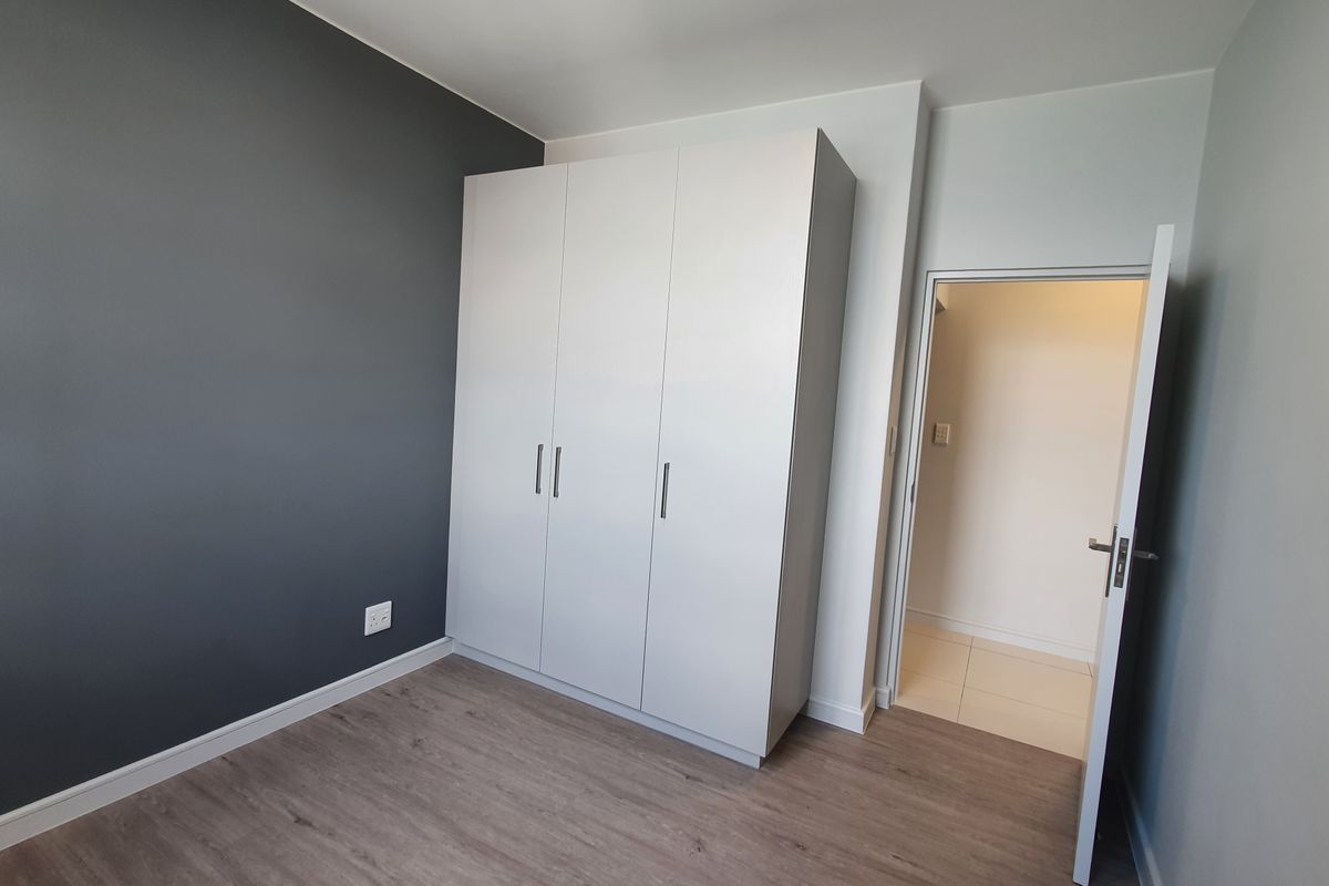 A clean, modern bedroom featuring light laminate flooring, a dark grey accent wall, and a large white built-in wardrobe.