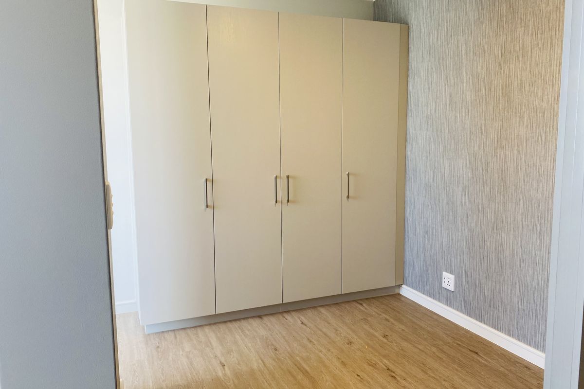 A clean, empty bedroom featuring modern laminate flooring, a large built-in wardrobe, and a feature wall with textured wallpaper.