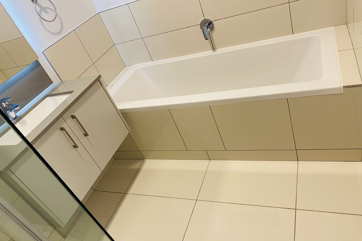 A clean, modern bathroom featuring a built-in bathtub, wall-mounted mixer, and a vanity cabinet with a stone countertop.
