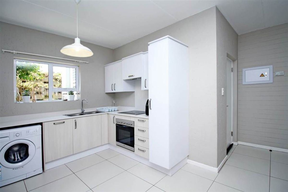 A clean, modern kitchen featuring light-toned cabinetry, built-in oven and hob, stainless steel sink, and neutral tiled flooring.