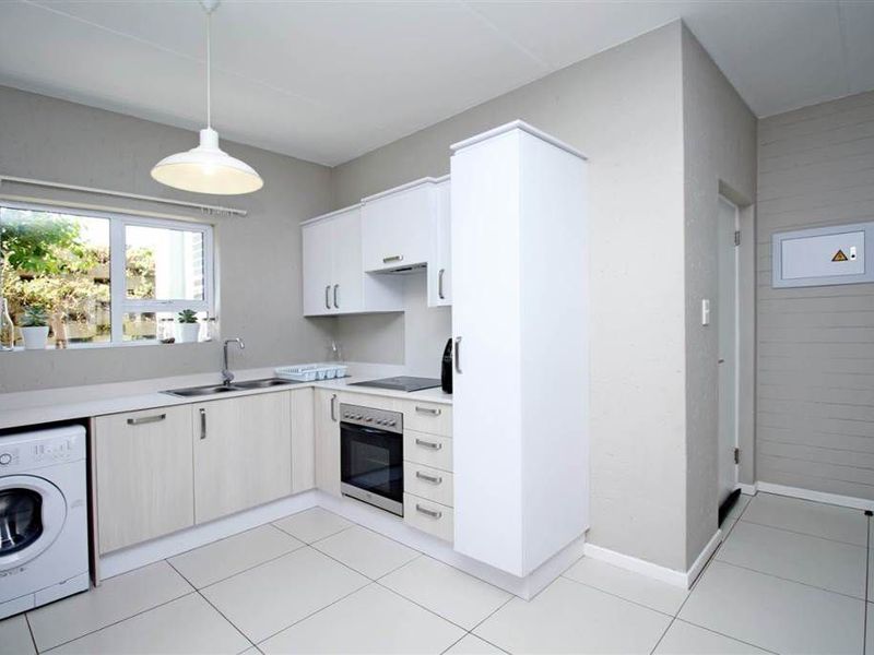 A clean, modern kitchen featuring light-toned cabinetry, built-in oven and hob, stainless steel sink, and neutral tiled flooring.
